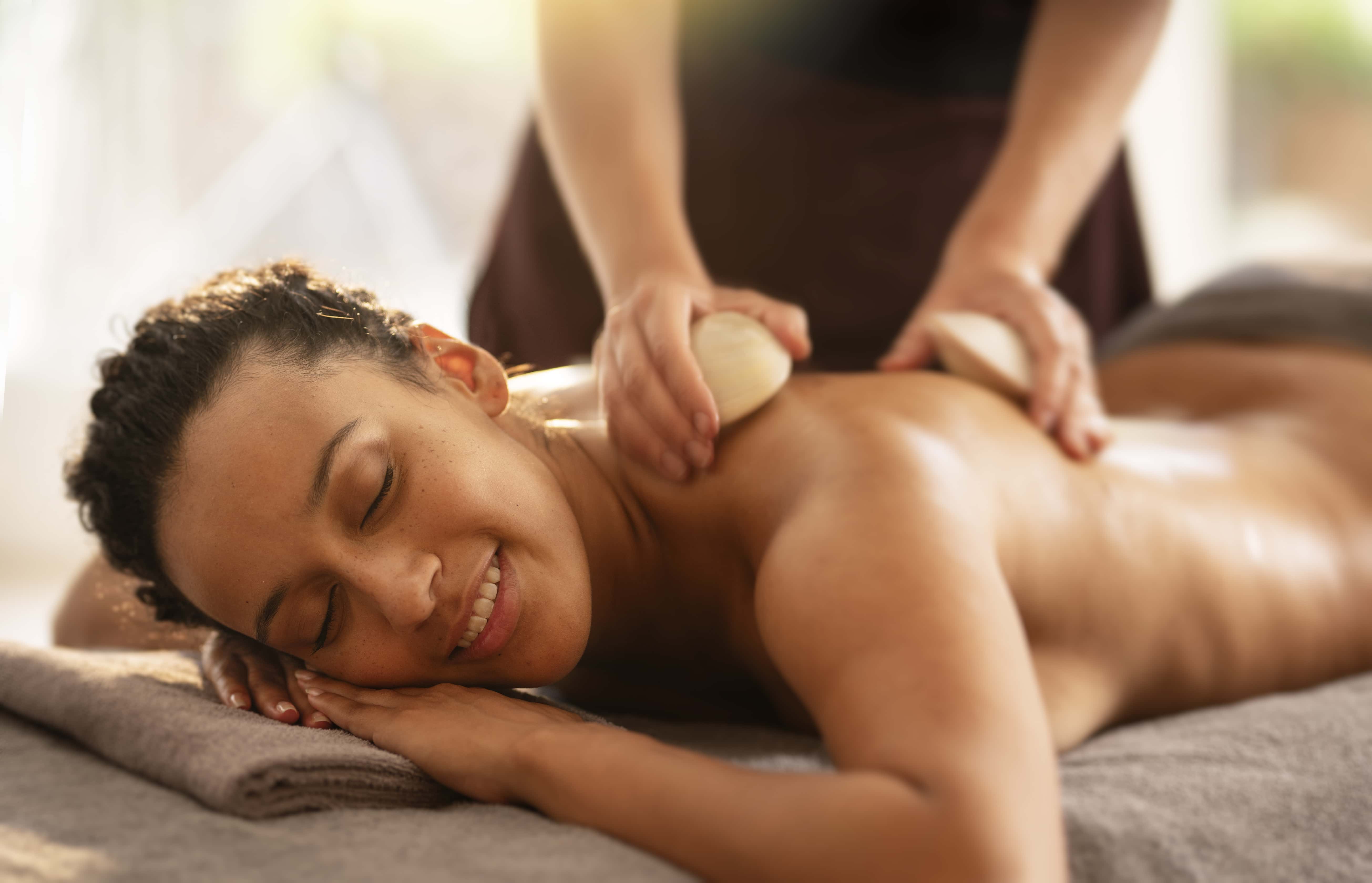 Femme allongée sur le ventre recevant un massage avec un coquillage chaud Alliance Pornic