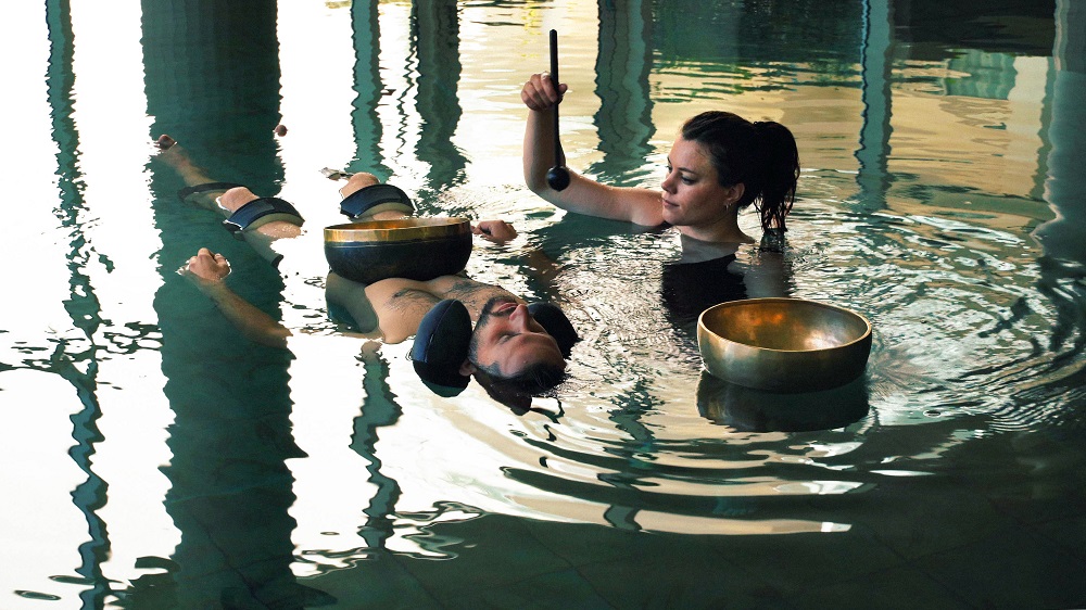 Homme flottant dans l'eau avec thérapeute à côté avec bols tibétains pour un Tao de l'eau Alliance Pornic